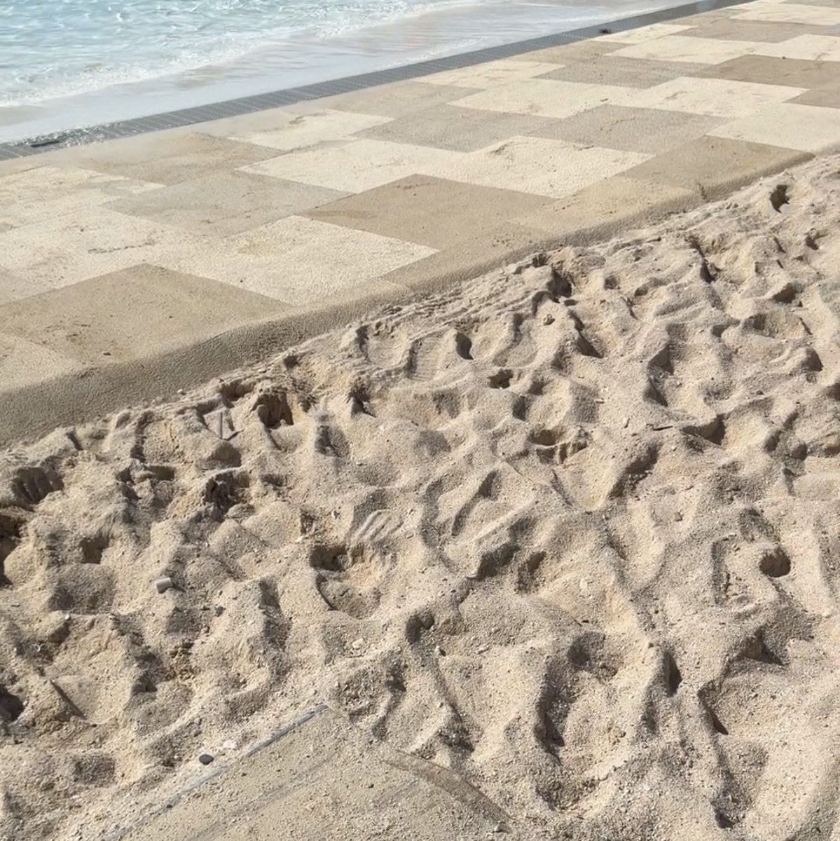 The end of the beach mat at Calypso Lagoon, with a stretch of loose sand before the paved lagoon walkway