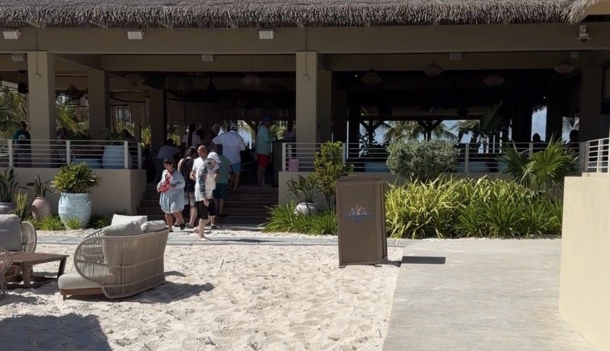 Pearl Cove Beach Club restaurant pavilion under a thatched roof, with a paved path beside the sand