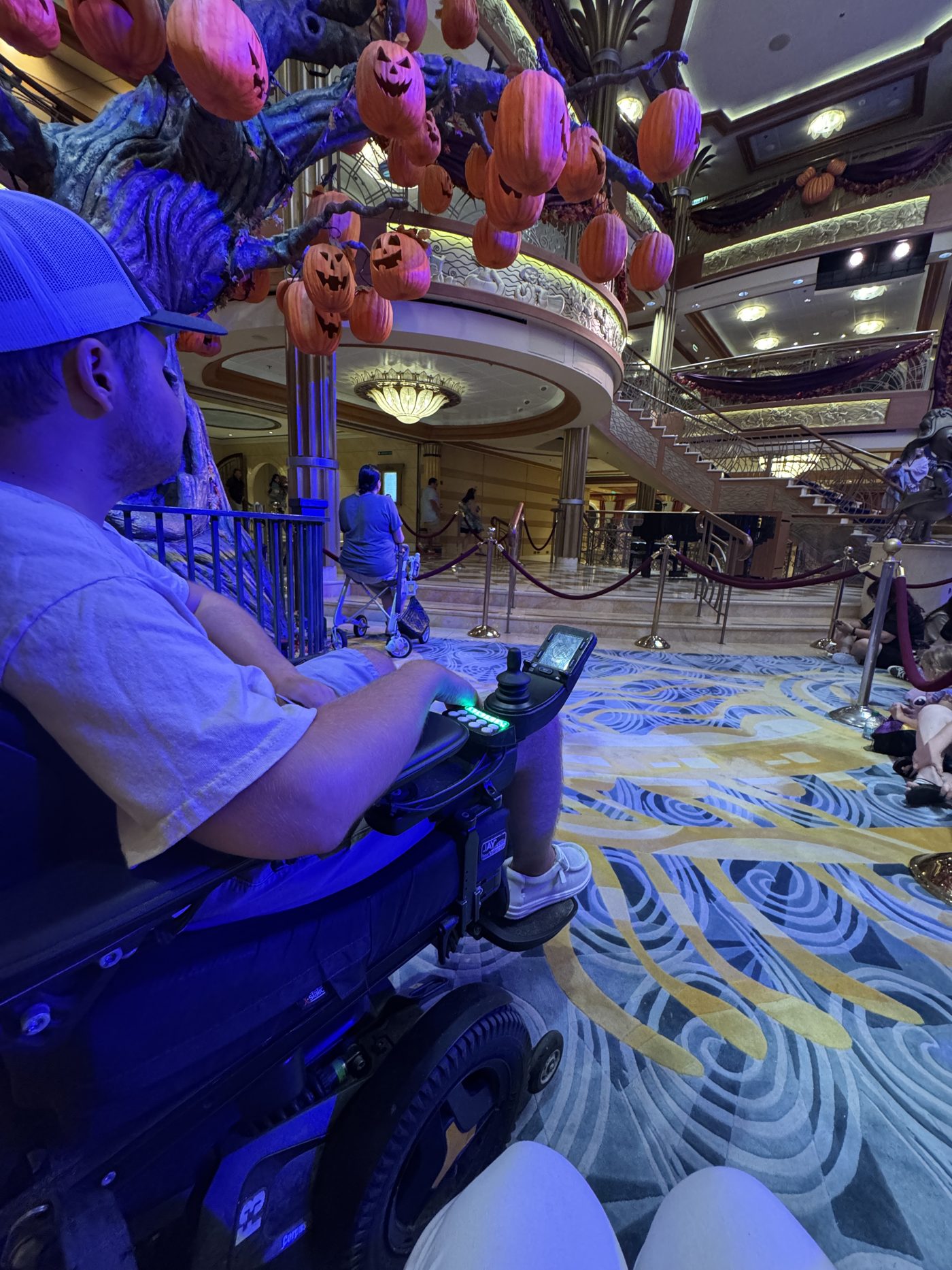 A guest using a power wheelchair in a Disney Cruise Line atrium, with clear pathways around entertainment and gathering areas