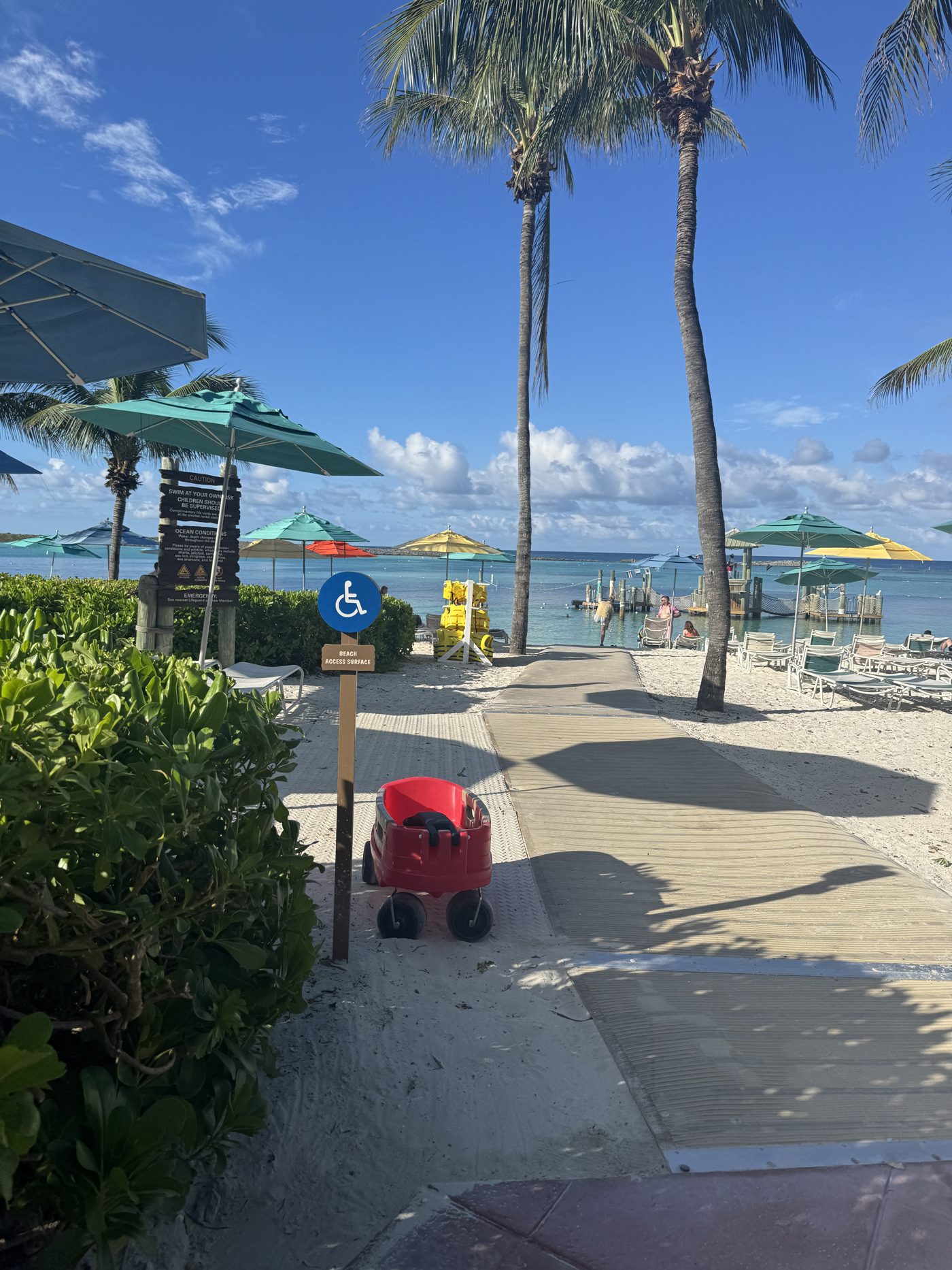 Mobi-mat pathway leading from the boardwalk across the sand to the beach at Castaway Cay, with a beach wheelchair parked at the accessible-access sign