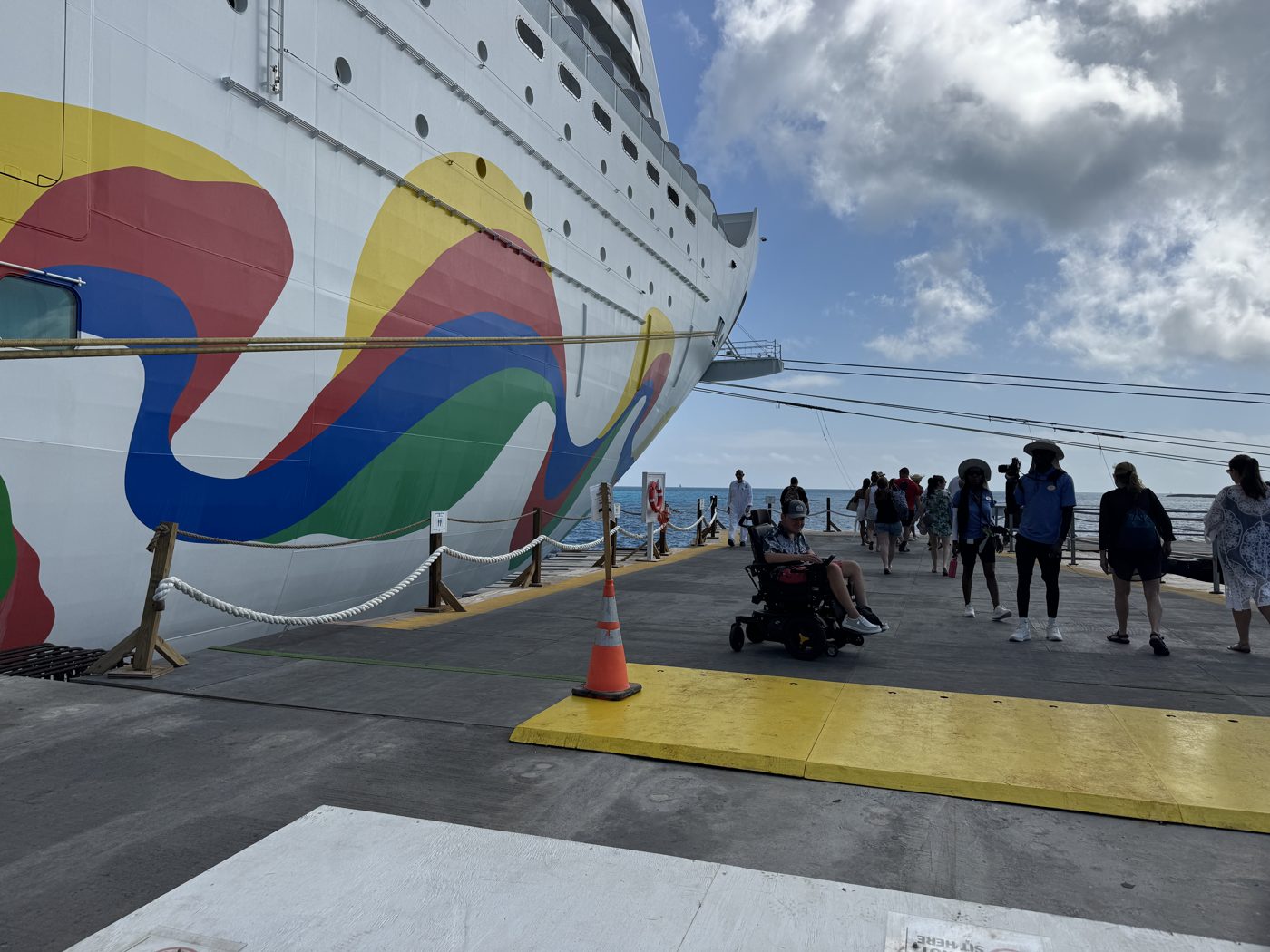 A traveler using a power wheelchair disembarking directly onto the pier at Great Stirrup Cay, rolling off the ship alongside other guests